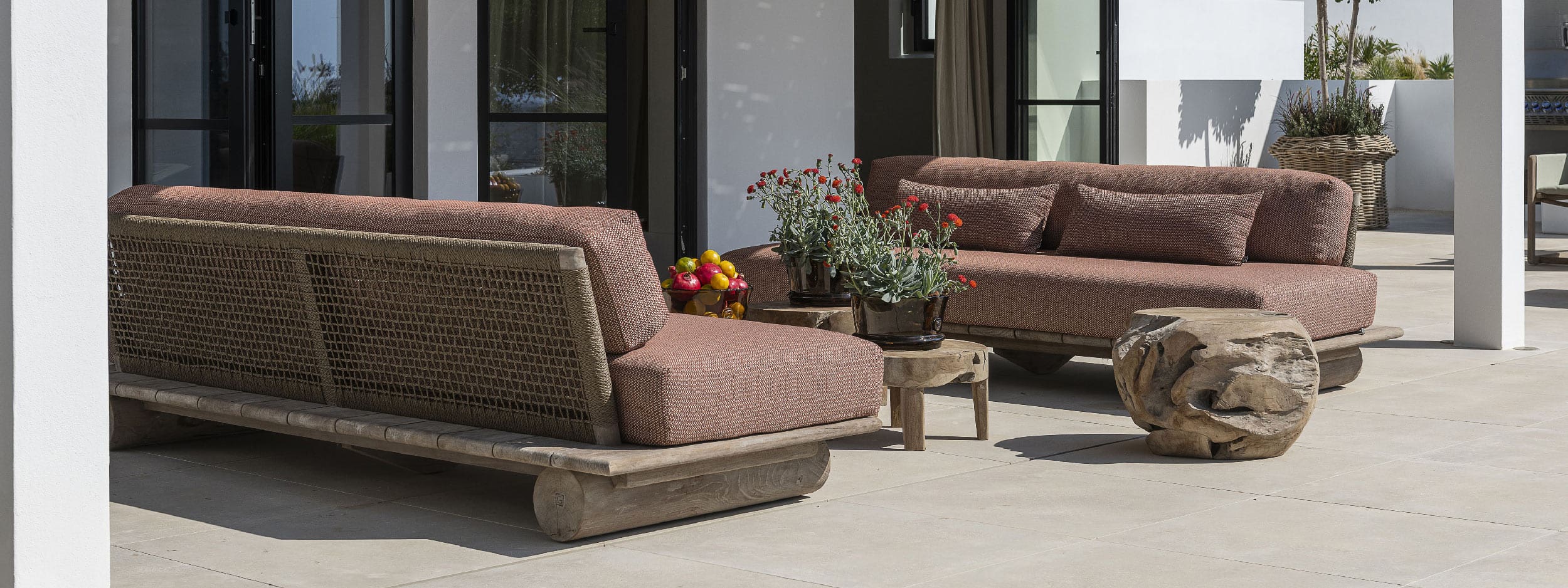 Image of pair of Gommaire teak garden sofas facing one-another on sunny white-washed terrace