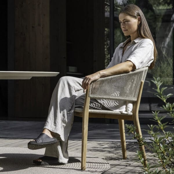 Image of contemplative woman sat in Cares teak carver chair by Royal Botania