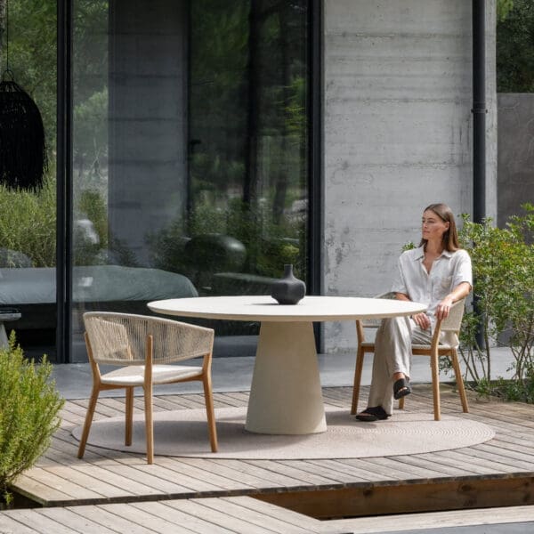 Image of woman sat in Royal Botania Cares chair next to Exes circular concrete table in Desert finish