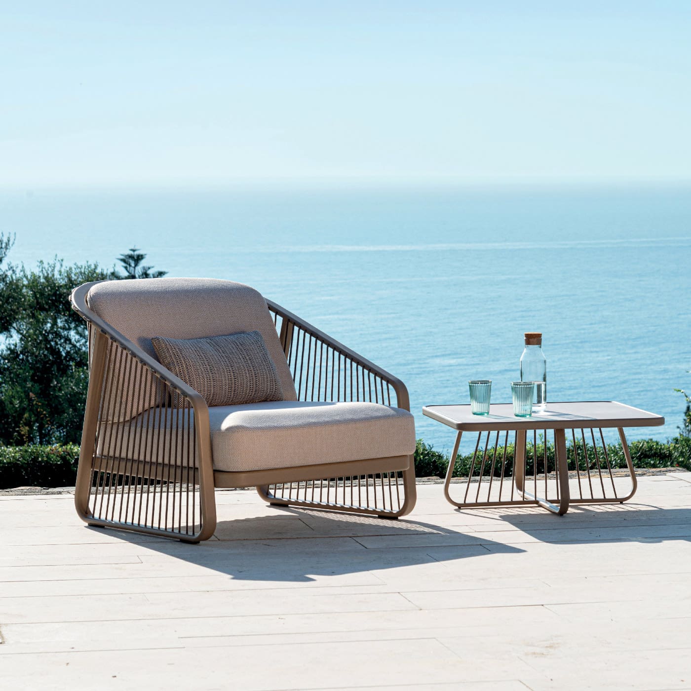 Image of Coro Sally luxury garden armchair and side table on sunny Italian terrace with sparkling sea in the background