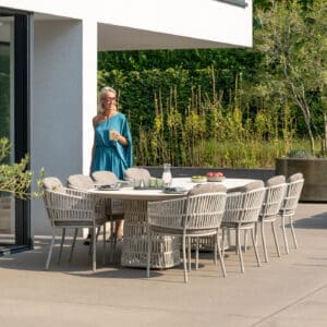 Image of woman in flowing turquoise dress stood next to Cala luxury garden dining set by Jati & Kebon