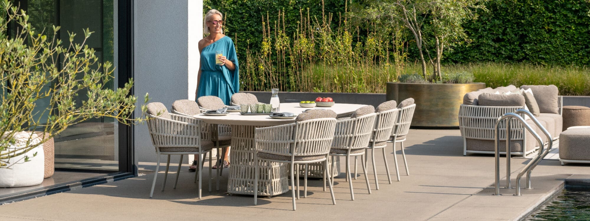 Image of woman stood next to Cala luxury garden dining furniture in natural tones by Jati & Kebon