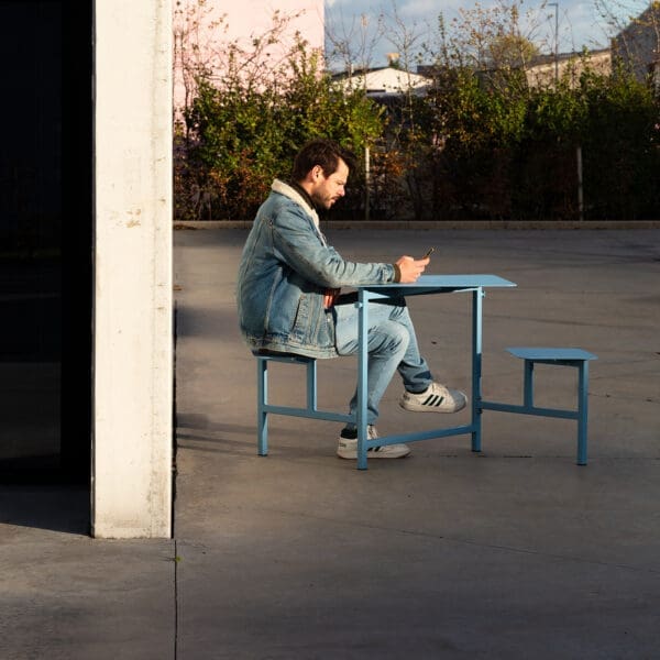 Image of young man sat looking at his phone whilst sat on teale-coloured The Duo mini picnic table by Wunder