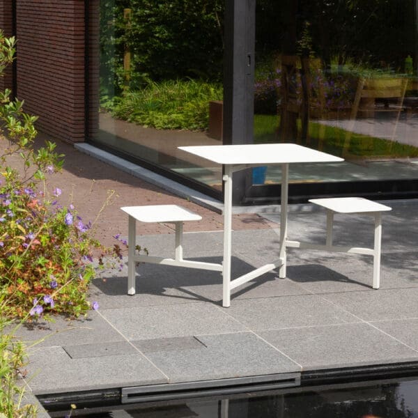 Image of white The Duo mini picnic table and seats for 2 on a terrace in front of still waters of a water feature
