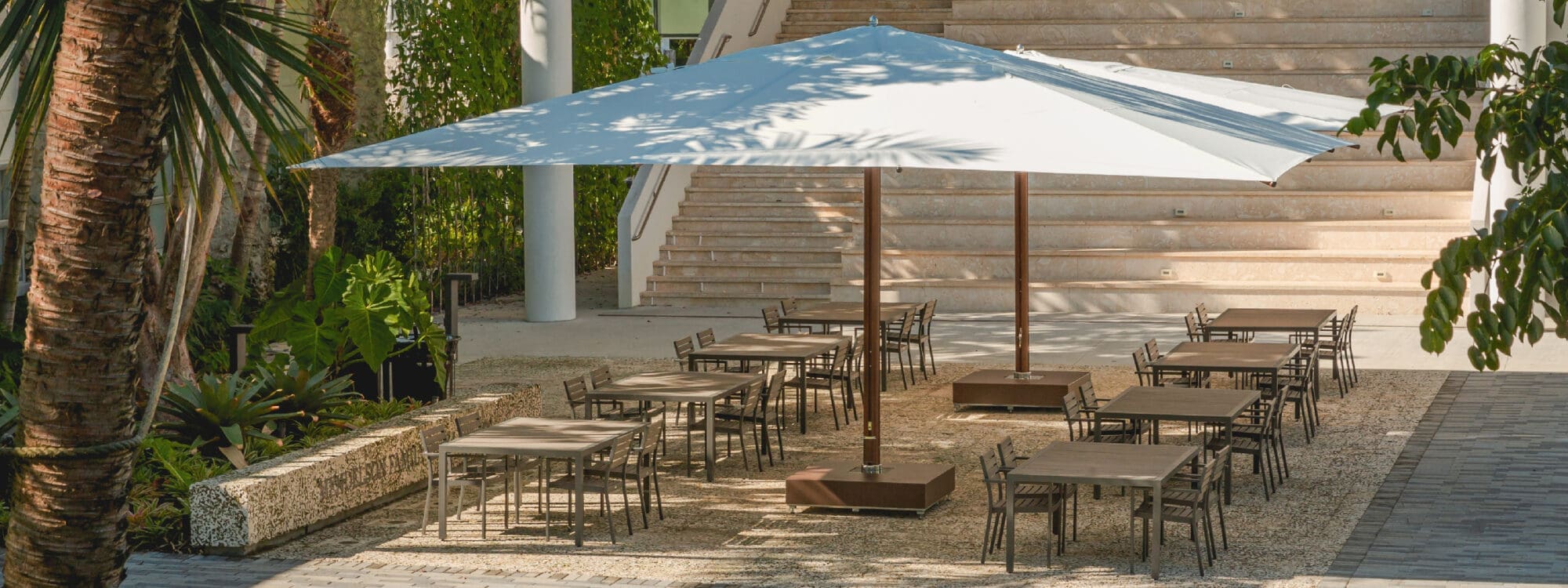 Image of pair of Tuuci Ocean Master Mega Max large parasols over multiple outdoor dining tables & chairs