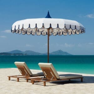 Image of pair of Tuuci Luma luxury sun lounges on a sandy beach beneath Voilare parasol and cloudless blue sky
