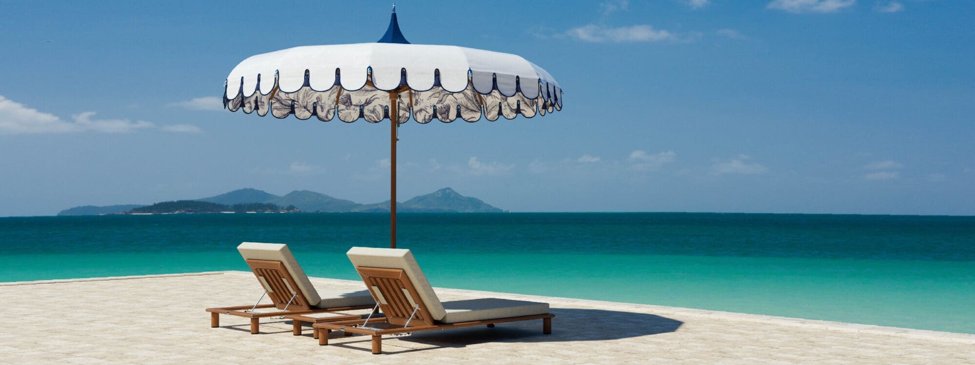 Image of pair of Tuuci Horizon sun loungers beneath a Ocean Master M1 Voilare Wonder parasol, on a hot, sunny and sandy tropical beach