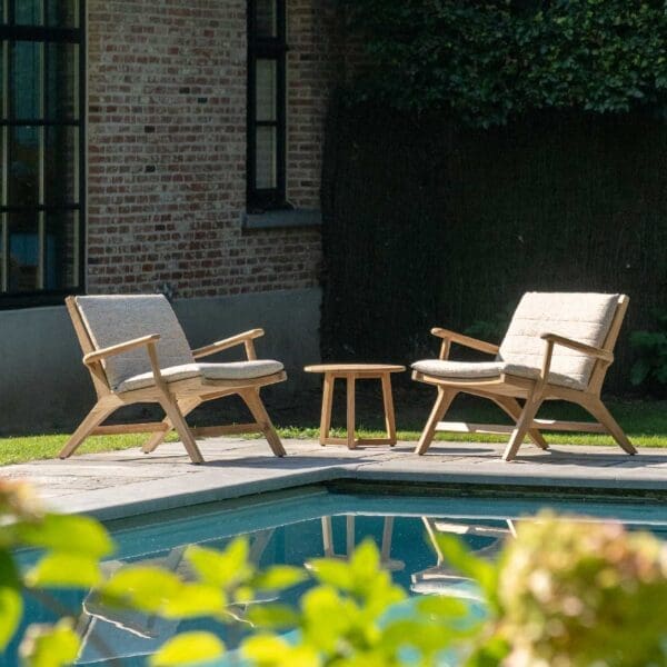 Image of a pair of Koozy teak armchairs beside the still waters of a swimming pool.