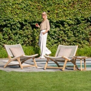 Image of a woman walking past a couple of Koozy teak garden lounge chairs by Jati & Kebon