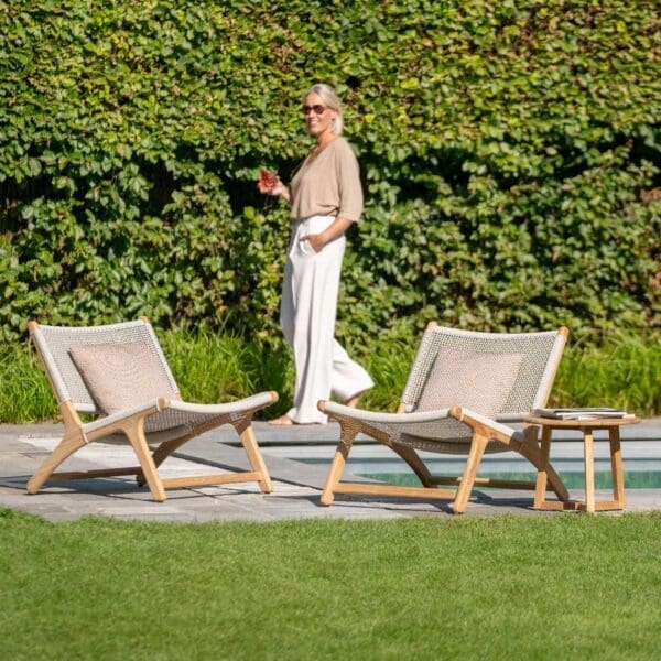 Image of a woman walking past a couple of Koozy teak garden lounge chairs by Jati & Kebon