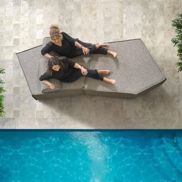 Image of bird's eye view of couple lying on a grey Anoko chaise longue next to the azure waters of a swimming pool