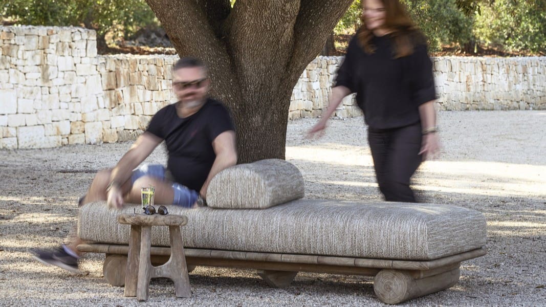 Image of a man sat on Gommaire Edge lounger beneath a tree with woman approaching from behind