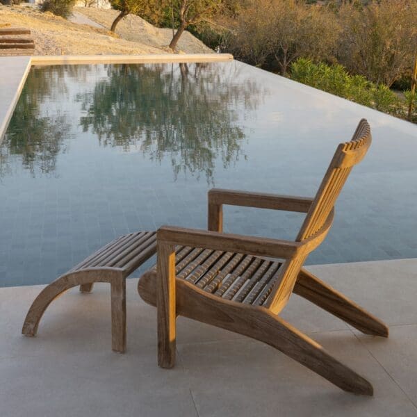 Image of Gommaire Orso contemporary teak easy chair and footrest beside still reflective waters of a swimming pool