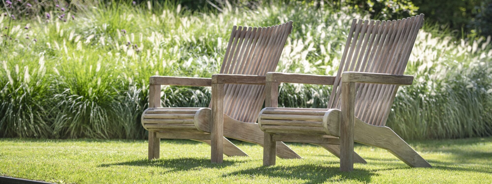 Image of pair of Gommaire Orso teak easy chairs on sunny lawn overlooking still waters of a pond