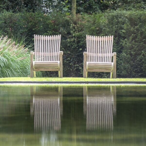 Image of pair of Gommaire Orso modern teak adirondack chairs reflecting in the water of still pond