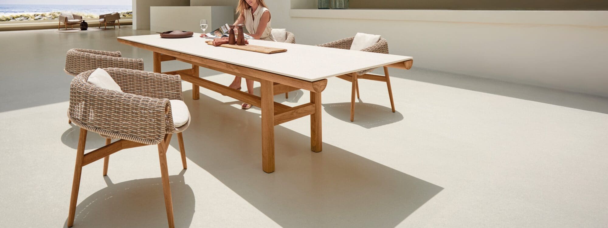 Image of woman sat in Gloster Wrap dining chair next to Rail teak garden table